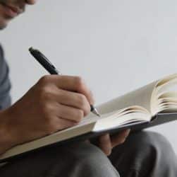 Homme assis ecrivant sur un carnet ouvert